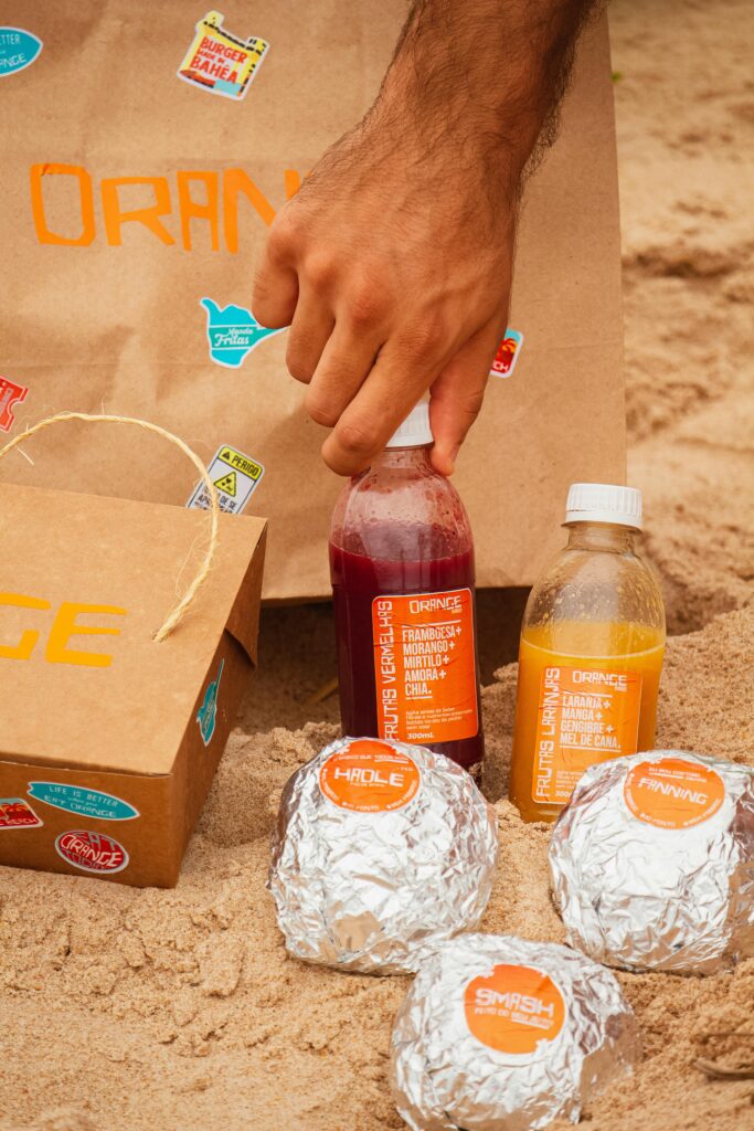 A casual picnic setup with drinks and wrapped food items on a sandy beach for a summer outing.